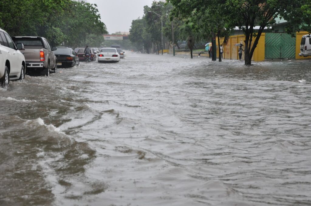 Carros varados en una calle inundada por intensas lluvias en República Dominicana, escenario de riesgo para conductores y peatones.